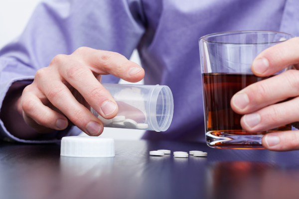 Man with alcoholic drink in one hand and pouring pills onto a table with other hand. Photo shows hands only.