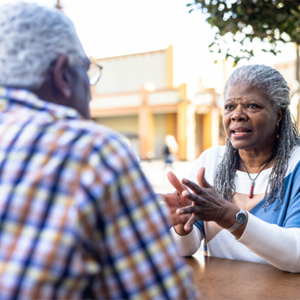 Two older adults sitting at an outdoor table talking