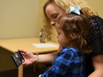 Toddler sitting in adult's lap looks at autism app on mobile phone