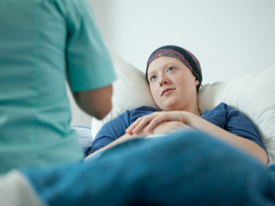 Cancer patient in bed with provider sitting at bedside (stock)