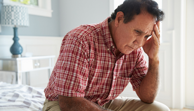 Older man sitting on bed looking sad