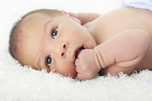 Baby lying on back on fuzzy surface with hand in mouth