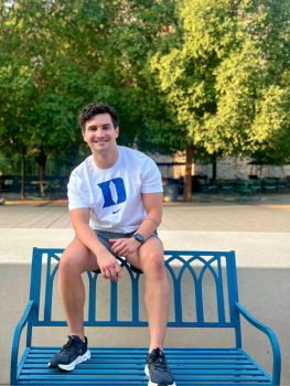 Andres Fuenmayor sitting on top of a blue bench, wearing a Duke t-shirt