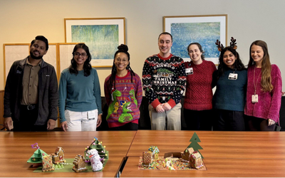 Seven people standing behind a table where there are two gingerbread houses displayed
