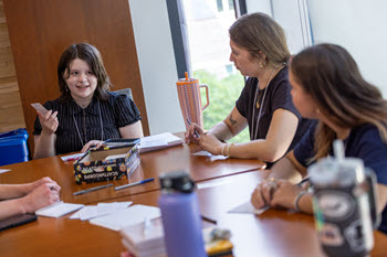 Several young adults engage in conversation around a conference room table
