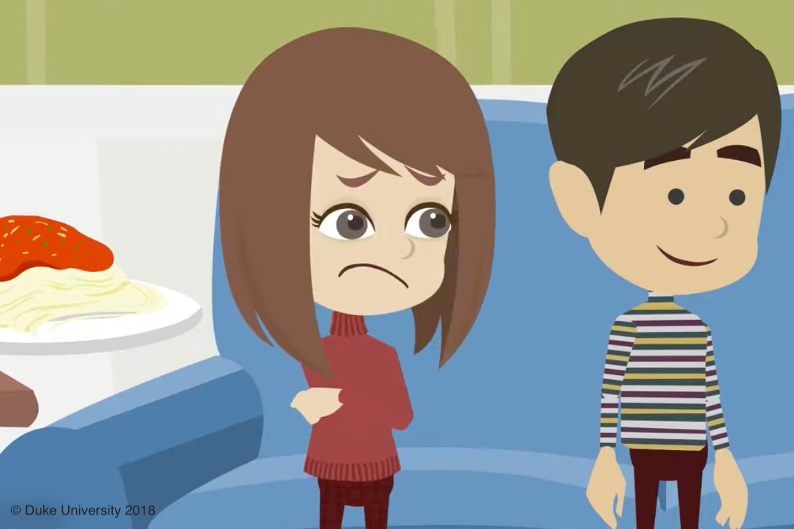 girl and boy standing next to each other, there is a plate of pasta next to the girl. Girl has an uncomfortable facial expression, boy has a smile on his face because he's not as bothered by the food