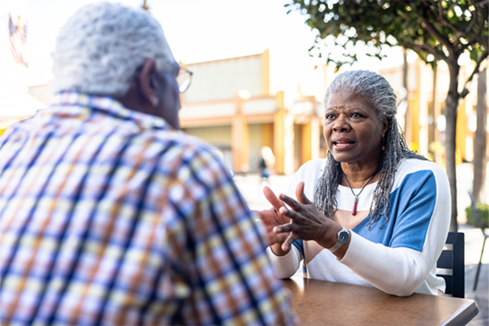 Two older adults sitting at an outdoor table talking