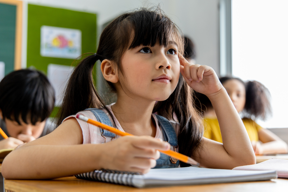 Young girl holding pencil and looking pensive in a classroom setting