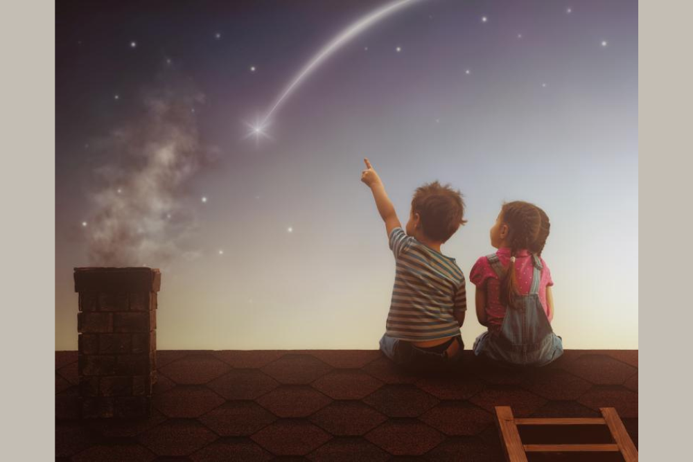 Two young children sitting on a rooftop with a shooting star falling. One child is pointing to the shooting star.