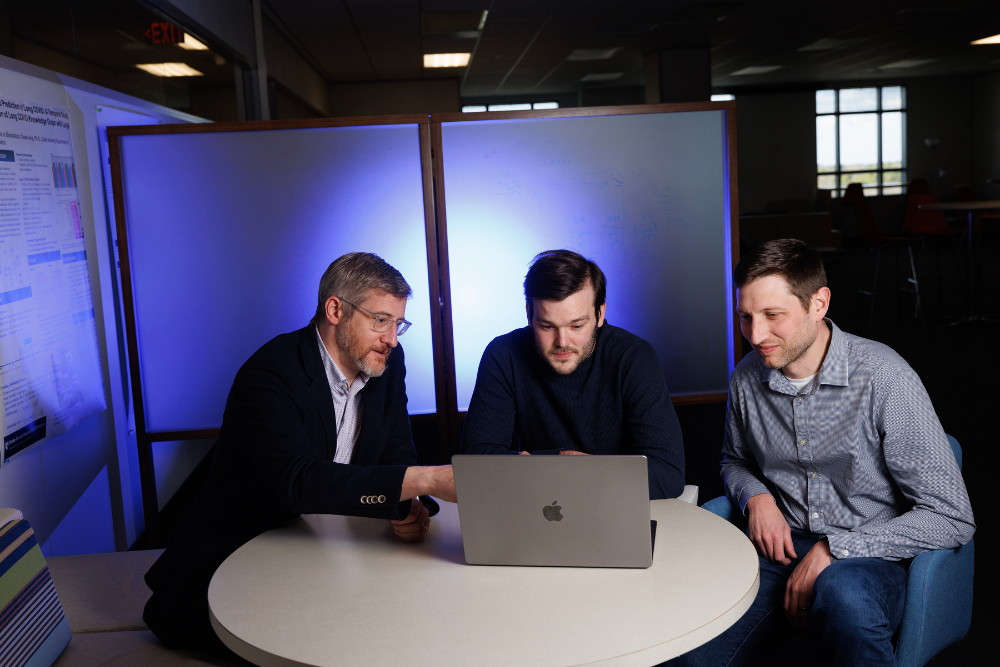 Jonathan Posner, Elliot Hill, and Matthew Engelhard look at a laptop together in a dark conference room..