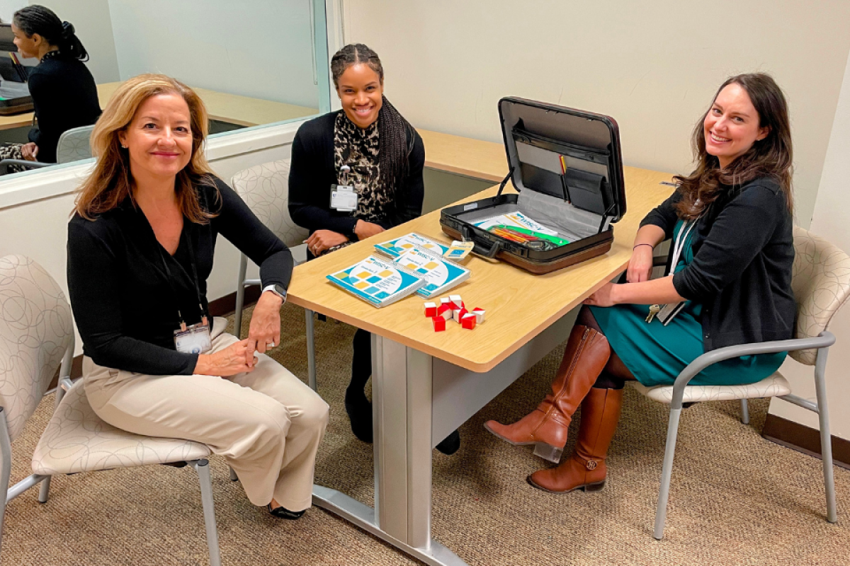 Three researchers pose for a photo with some of the materials used to perform cognitive evaluations with children.