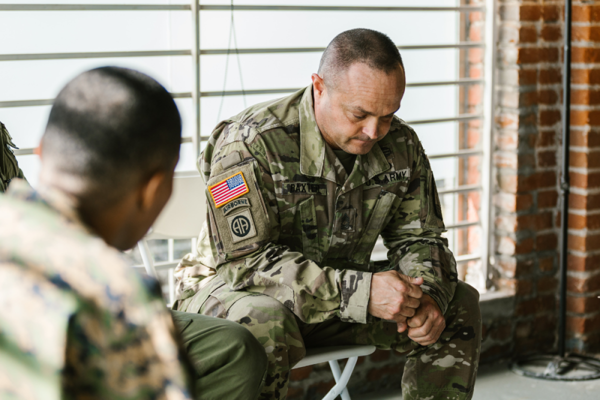 Man in camouflage military uniform sitting in front of a window with head down