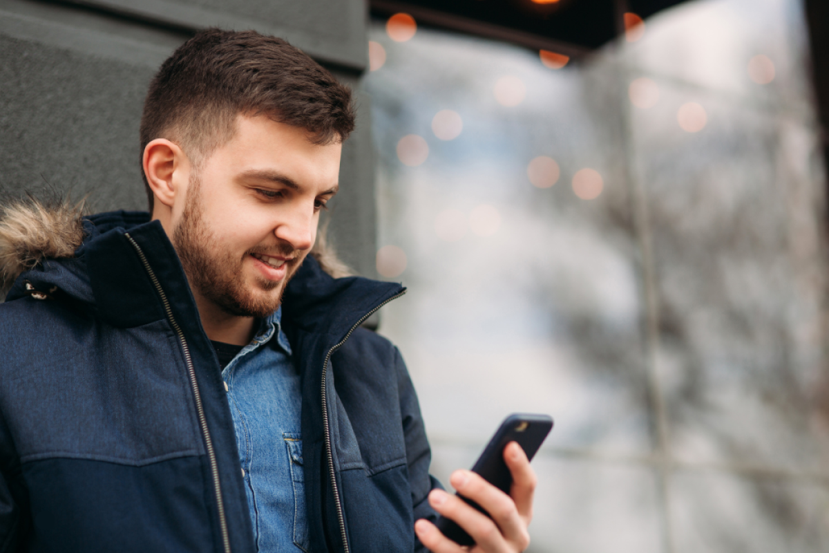 Young man in parka standing outside looking at his cell phone