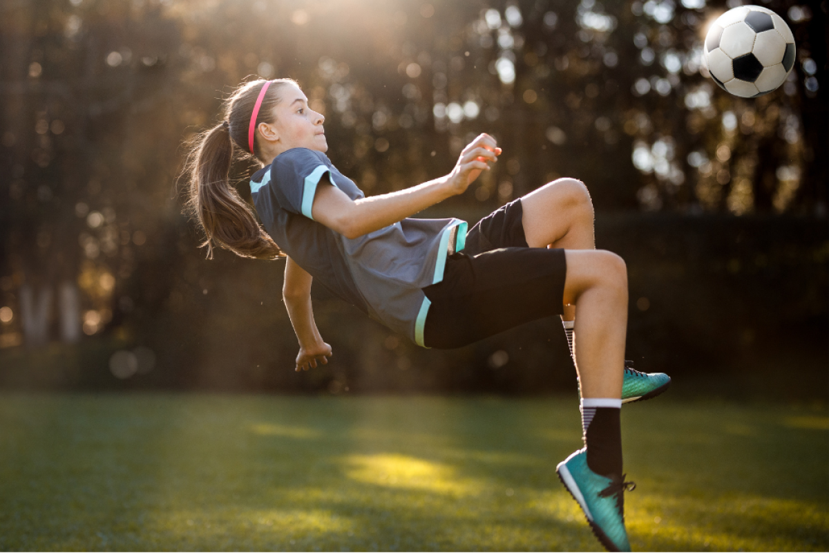 Young girl playing soccer about to hit the ball with her knee; she appears to be off balance and about to fall.