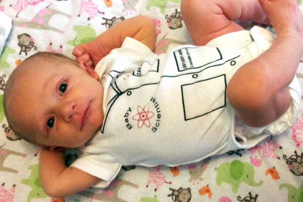 Very young baby lying on back on colorful baby mat in "Baby Scientist" onesie