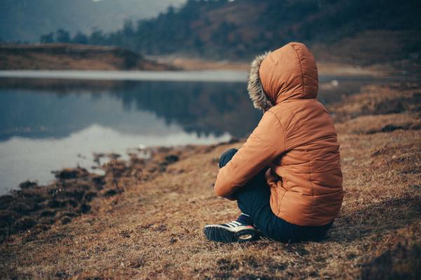 Girl with hooded jacket sitting down looking at water