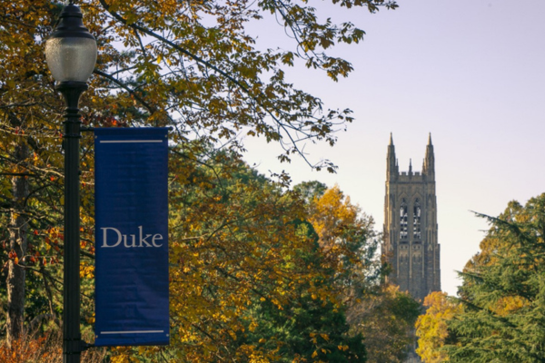 Duke sign with top of Duke Chapel in background. Leafy trees (fall).