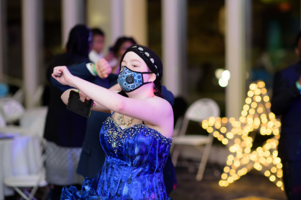 Teenager in shiny blue dress with mask and hat dances at a recent Duke Children's prom