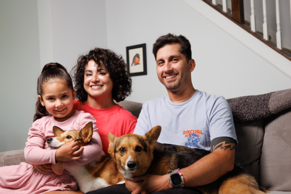 Man and woman sitting on couch with young girl and two dogs on their laps.