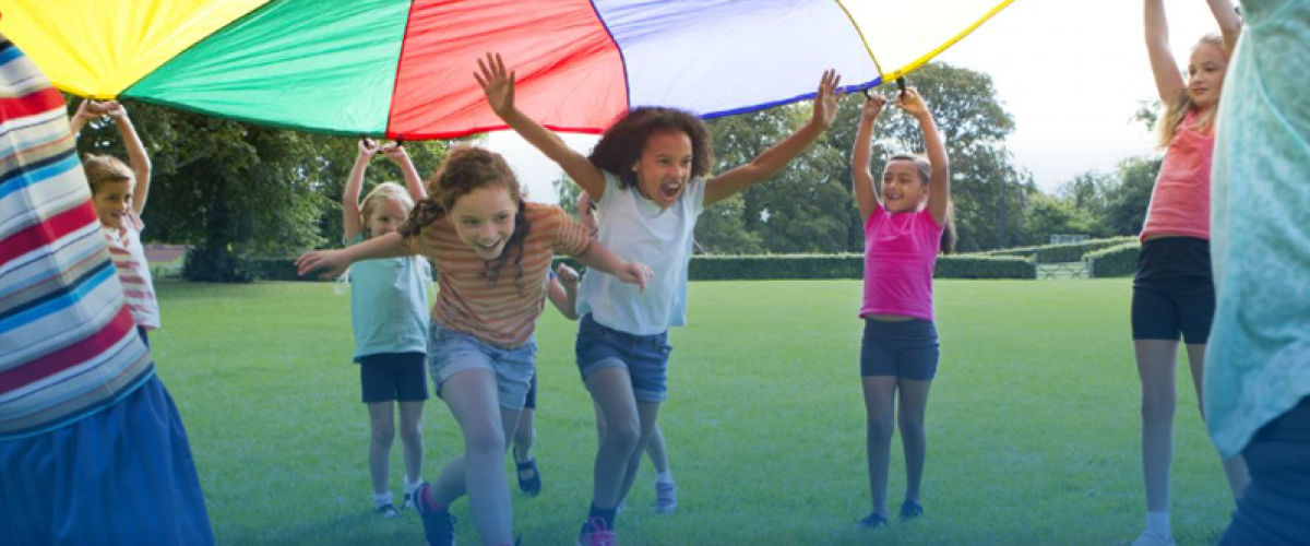children in a field running under a colorful parachute