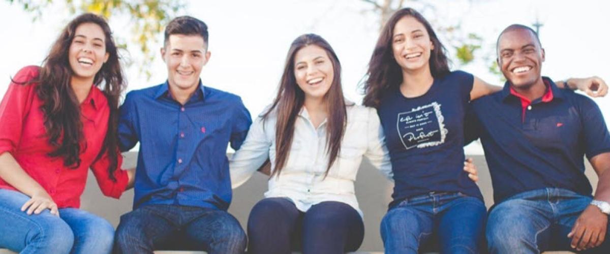 Five men and women sitting on a bench with arms around each other and smiling