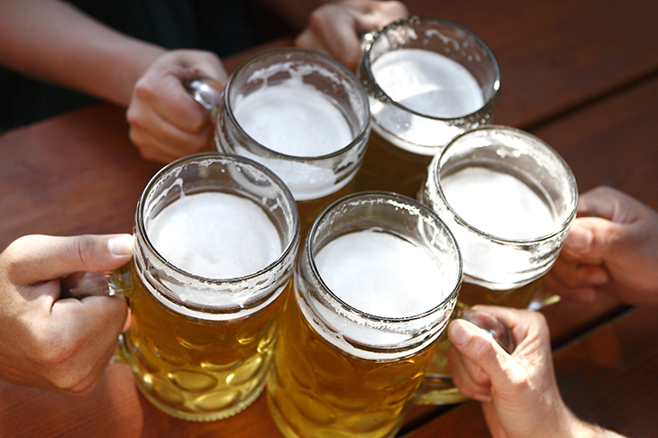 Five glass mugs filled with beer, people doing "cheers"