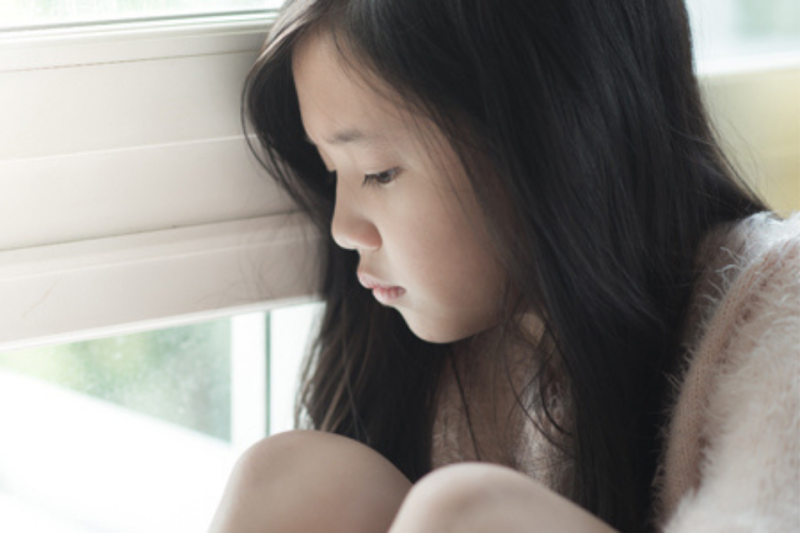 Young girl looking sad, looking out the window