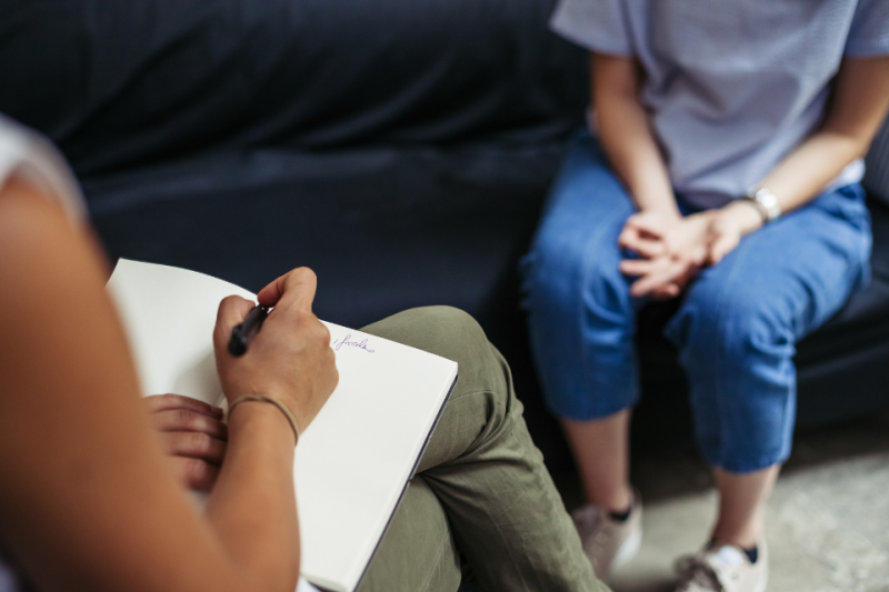 Therapist and teenager/young adult in therapy session. No faces showing.