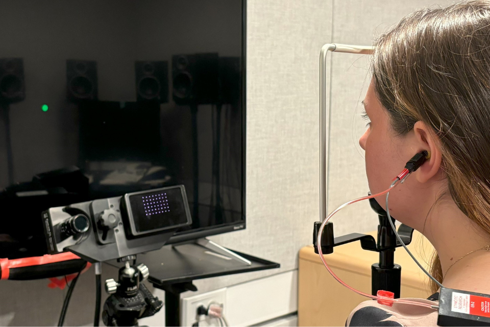 Woman with earbuds looking at black screen with small green dot on screen. 