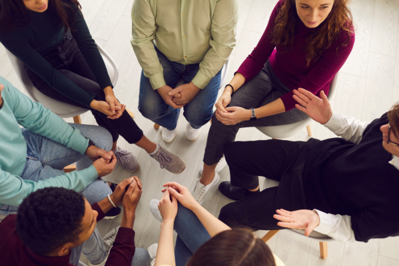 Young adults engaged in group therapy (view from above, faces not showing)