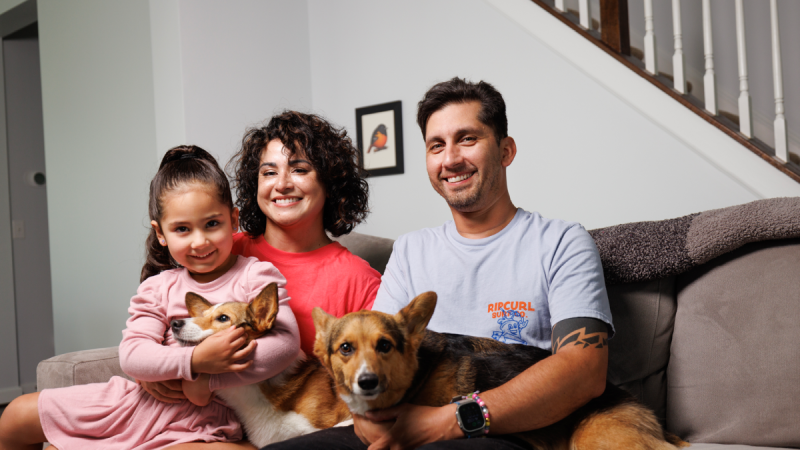 Man and woman sitting on couch with young girl and two dogs on their laps.