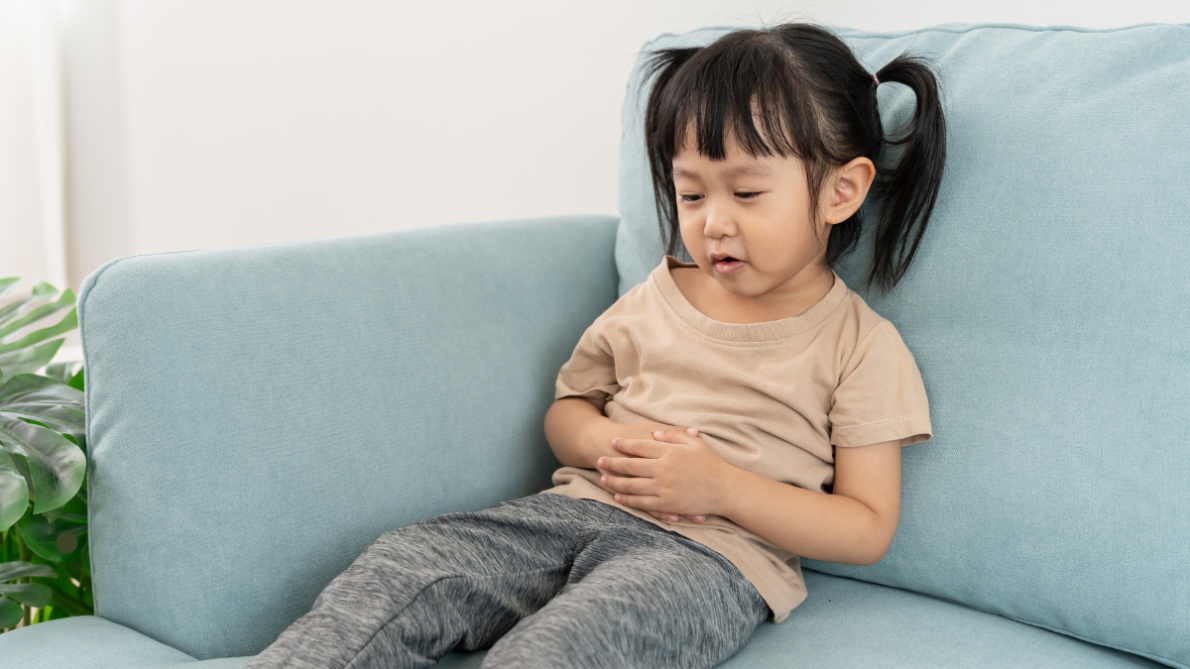Young girl holds stomach while lying on blue couch