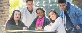 Five teenage friends sitting/standing at table outdoors
