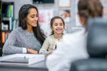Doctor (back to camera) talks with young girl and her caregiver (woman)
