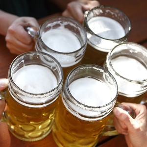 Five glass mugs filled with beer, people doing "cheers"