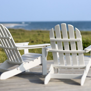 Two white Adirondack chairs facing a green field and body of water