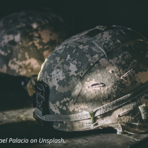 Two military helmets; dark background. Photo by Israel Palacio on Unsplash.