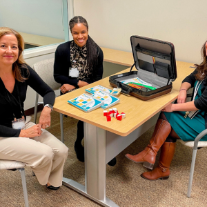 Three researchers pose for a photo with some of the materials used to perform cognitive evaluations with children.