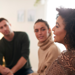 Three people talking in a group therapy setting. Fourth person on far left is cut off.
