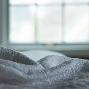 Rumpled bed linens in dark room; window in background