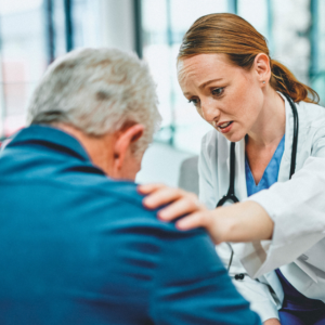 Concerned-looking doctor with hand on patient's shoulder. Patient facing away from camera.