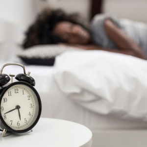 Alarm clock in foreground; woman sleeping on white sheets in background