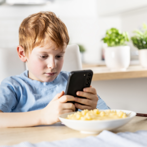 Child with bowl of mac & cheese; distracted by cell phone; not eating