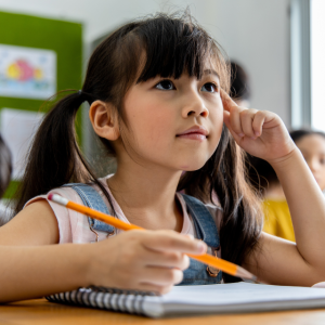 Young girl holding pencil and looking pensive in a classroom setting