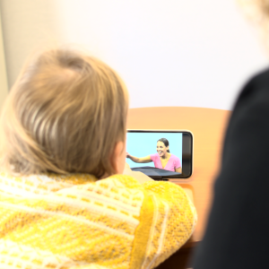 Toddler looking at phone screen with woman sitting behind her (view from behind)
