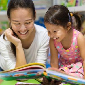 Woman and child smiling and reading together in what appears to be a children's library