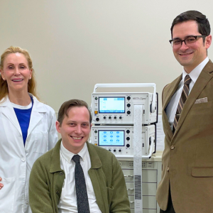 Grace Gunderson-Falcone, Johnny Komisar, and Jake Feigal pose around an ECT machine.