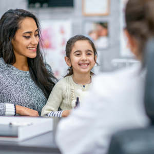 Doctor (back to camera) talks with young girl and her caregiver (woman)