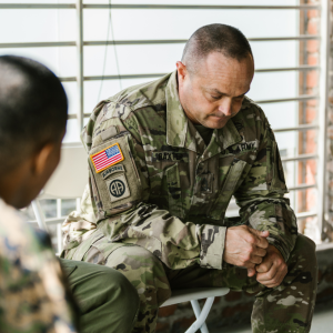 Man in camouflage military uniform sitting in front of a window with head down
