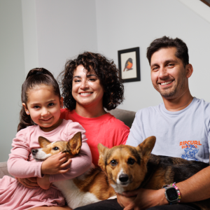 Man and woman sitting on couch with young girl and two dogs on their laps.